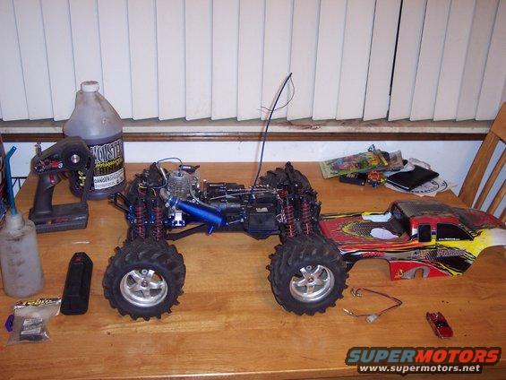 Remote-controlled monster truck with a detached body, on a wooden table with a controller and fuel bottle