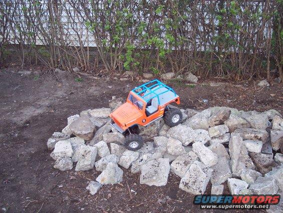 Orange toy remote control vehicle with a blue roll cage on a pile of rocks