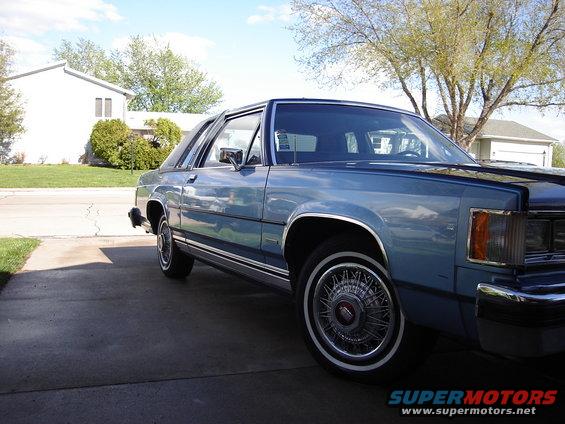 Blue sedan parked in driveway, front quarter view. Has wire-spoke wheels and chrome trim