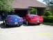 2006 Ford Mustang - Two Ford Mustangs are parked in front of a garage. The blue Mustang is on the left and the red Mustang is on the right.