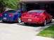 2006 Ford Mustang - Two Ford Mustangs, a red one and a blue one, are parked outside a garage.
