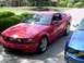 2006 Ford Mustang - A red 2006 Ford Mustang is parked in a driveway next to a blue vehicle, with a house in the background.