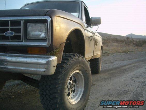 Close-up of a lifted Ford pickup truck with large tires on a dirt road