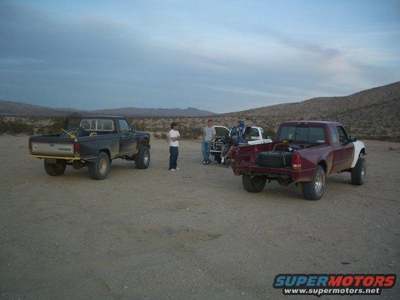 Three trucks parked in a desert landscape under a cloudy sky