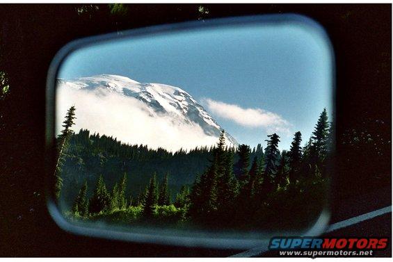 Mountain landscape reflected in a side mirror, with trees and clouds