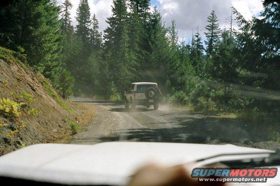 SUV kicking up dust on a winding dirt road through a forest