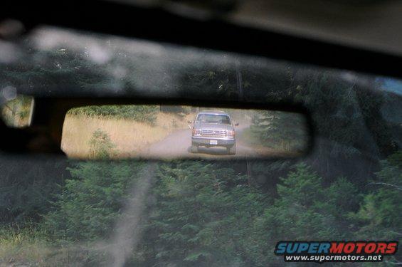 Silver pickup truck on a dirt road, seen in rearview mirror
