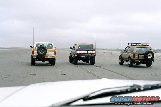 Three 1979 Ford Broncos driving on a beach, rear view
