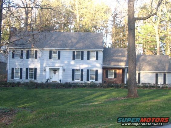 Light blue house with black shutters and a brick section, viewed from a grassy lawn