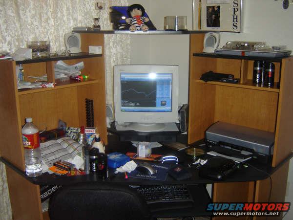 Desk setup with CRT monitor displaying a graph, keyboard, printer, and shelves with bottles and other items