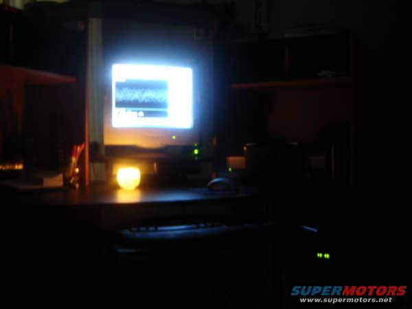 Computer monitor displaying a waveform, desk with a candle, and keyboard in a dark room