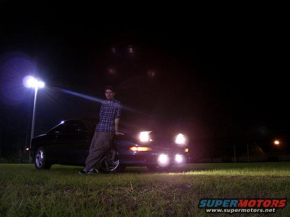 Dark 1994 Ford Probe front view at night with headlights on, person leaning on car