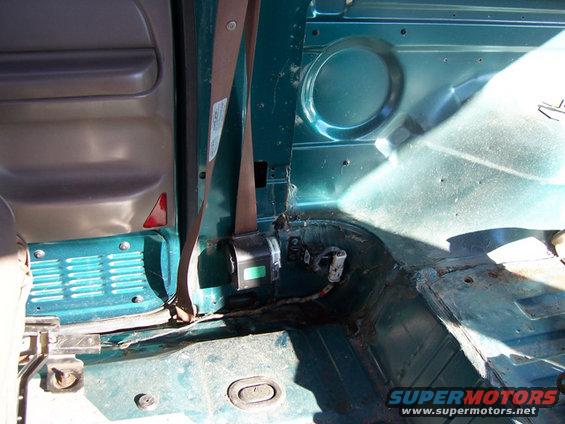 Interior of a vehicle showing the rear passenger side door panel, seatbelt mechanism, and floor area