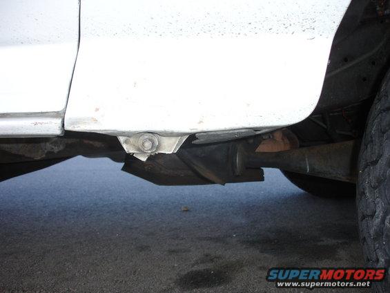 Close-up of the underside of a white vehicle, showing the frame and part of the exhaust system