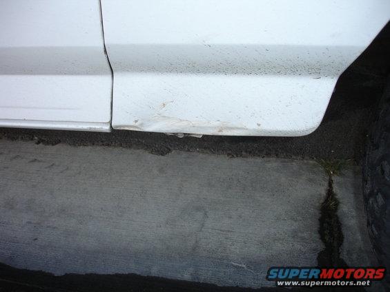 White vehicle lower body panel with dent and rust near the ground
