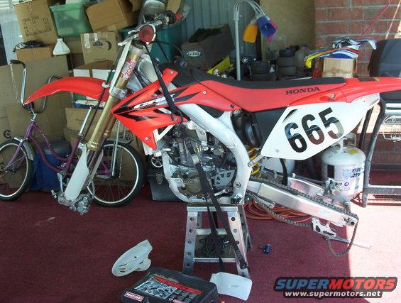 Red and white 2006 Honda CR250R dirt bike on a stand, number 665 on side panel