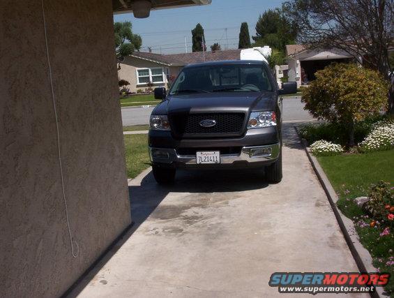 Front view of a dark gray Ford F-150 pickup truck parked in a driveway. License plate reads 7L21411