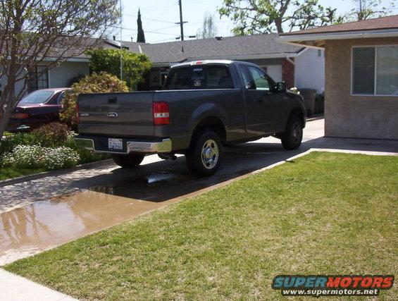 Gray Ford F-150 pickup truck parked in driveway next to a house. Another car is parked in the yard
