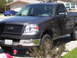 2006 Honda CR250R - A dark gray Ford F-150 pickup truck is parked in a driveway with a blue sports car in the background.