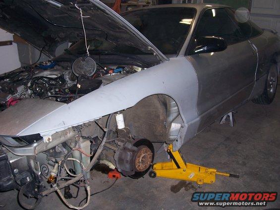 Silver car with hood open, undergoing repairs, front fender removed, on a yellow jack