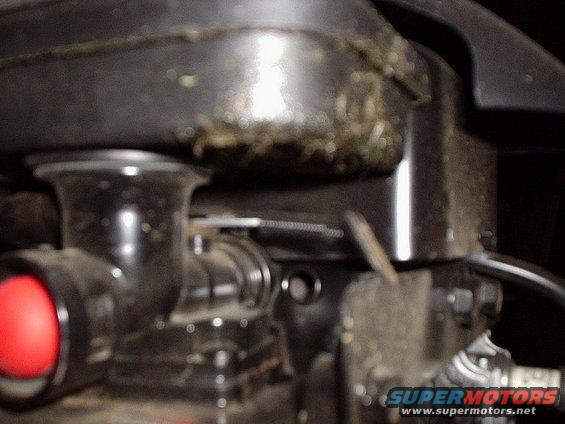 Black engine component with red circular element and grass debris on top