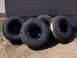 1996 Ford Bronco - Four Goodyear MTR tires with aggressive tread patterns are displayed on black rims, resting on dry grass in front of a building.