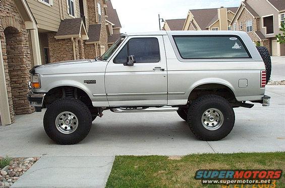 Silver 1996 Ford Bronco SUV parked on a driveway, side view, lifted suspension, aftermarket wheels, spare tire on rear door