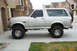 1996 Ford Bronco - A silver 1996 Ford Bronco SUV is shown from the side, parked in front of a residential building.