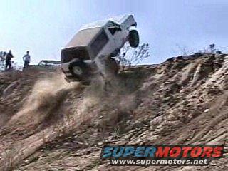 White SUV tumbling down a dirt embankment with people watching