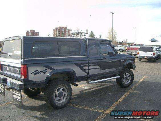 Dark blue Ford Ranger pickup with a camper shell and 4x4 graphics. Parked in a lot with other vehicles