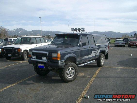 Dark blue 1992 Ford Ranger pickup truck with a camper shell, aftermarket wheels, and a light bar on the roof