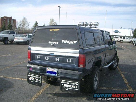 Rear view of a dark blue Ford pickup with a camper shell and mud flaps that say 'Big Sky Country Montana'