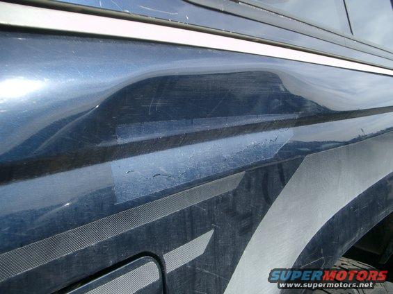 Close-up of a dented blue truck fender with tape repair and graphics