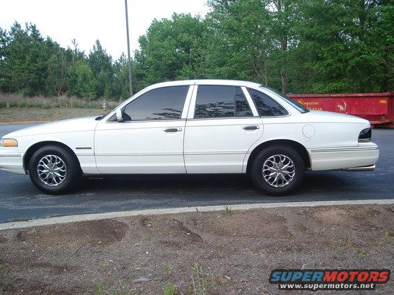 White 1995 Ford Crown Victoria sedan, side view, chrome wheels, tinted windows, parked on asphalt