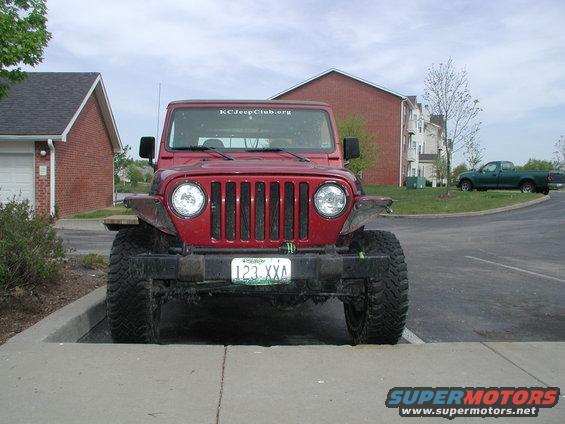 Red Jeep Wrangler parked on concrete, front view. Large tires, aftermarket bumper, KCJeepClub.org sticker on windshield