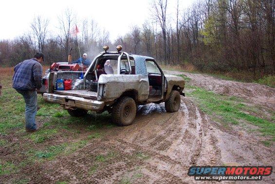 Mud-covered off-road vehicle with roll cage, open doors, and a man loading items into the bed
