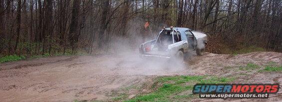 Off-road truck driving through mud and dust on a wooded trail