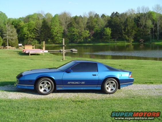 Blue IROC-Z Camaro parked on gravel by a lake
