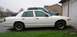 1998 Ford Crown Victoria - A white 1998 Ford Crown Victoria is parked in front of a garage, with a blue pickup truck behind it.
