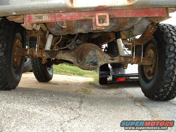 Rear axle, leaf springs, and shocks visible on a truck, with a trailer hitch receiver