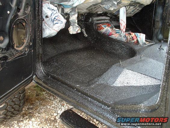 Interior of a vehicle with black spray-on bedliner material applied to the floor and lower door panels. Newspaper is stuffed into the dashboard area