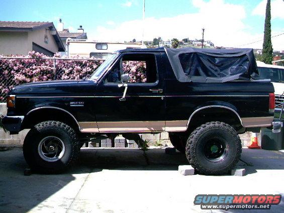 Black Ford Bronco with tan stripe, lifted, black soft top, side view