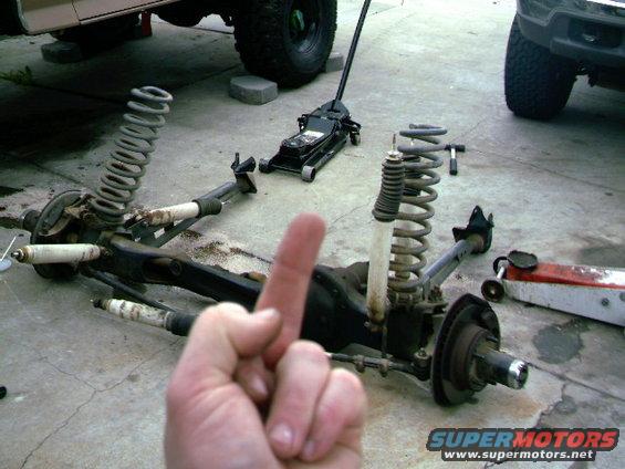 vehicle suspension parts on ground, jack nearby, another vehicle in background