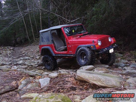 Red 2003 Jeep Wrangler on a rocky trail with a soft top