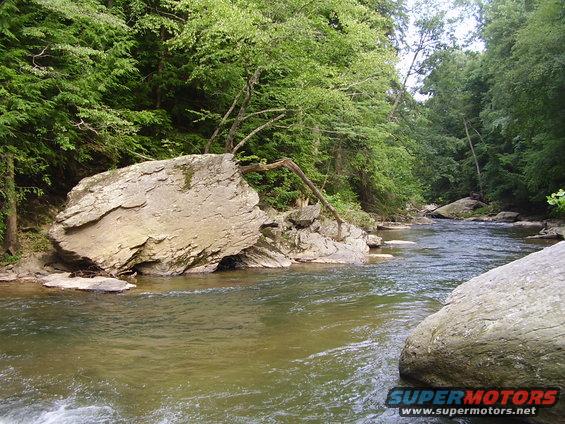 River flowing past large rocks and trees on a sunny day