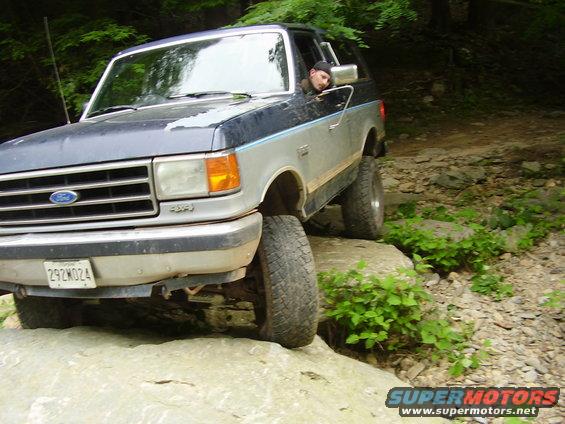 Ford Bronco on rocks, blue and silver, driver visible, license plate 292M024