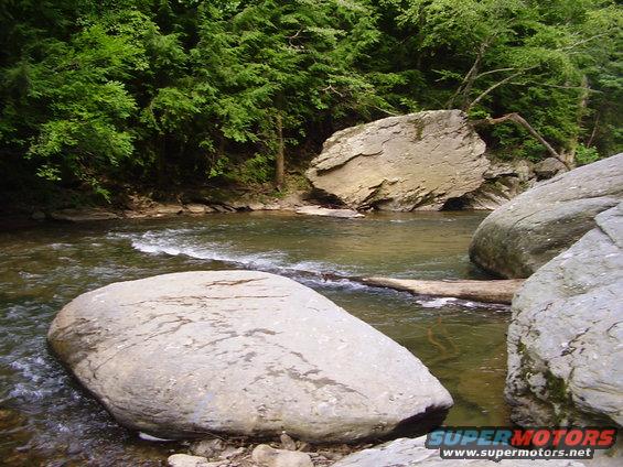 River flowing past large rocks with trees in the background