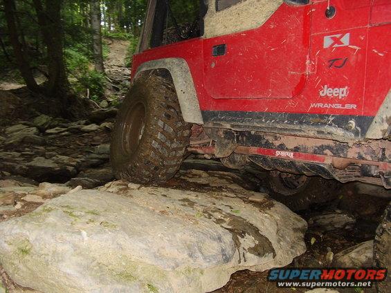 Red Jeep Wrangler TJ on rocky trail, front tire on large rock