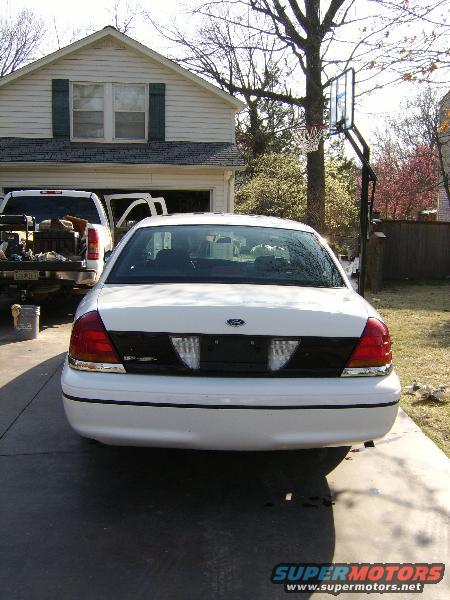 Rear of a white sedan parked in a driveway, with a pickup truck to the left
