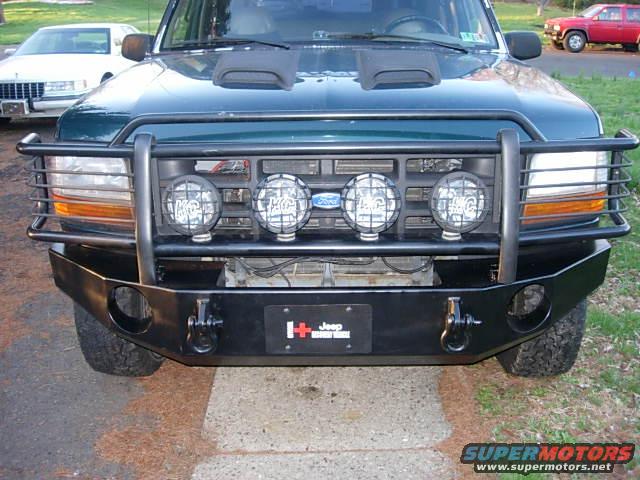 1993 Ford Bronco front view with aftermarket bumper, KC lights, and hood scoops. Another vehicle is parked to the left